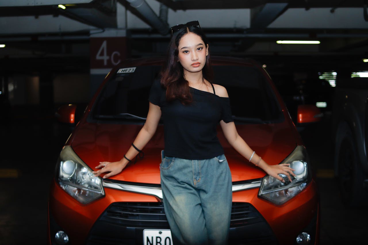 about-03 Stylish woman in a dark garage leaning on an orange car, exuding confidence.