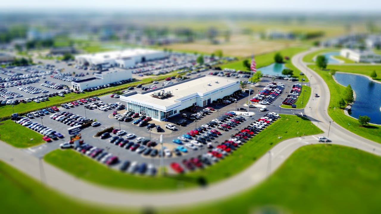 The Art of Drawing Readers In: Your attractive post title goes here Aerial high-angle view of a bustling car dealership surrounded by parked cars in a green landscape.