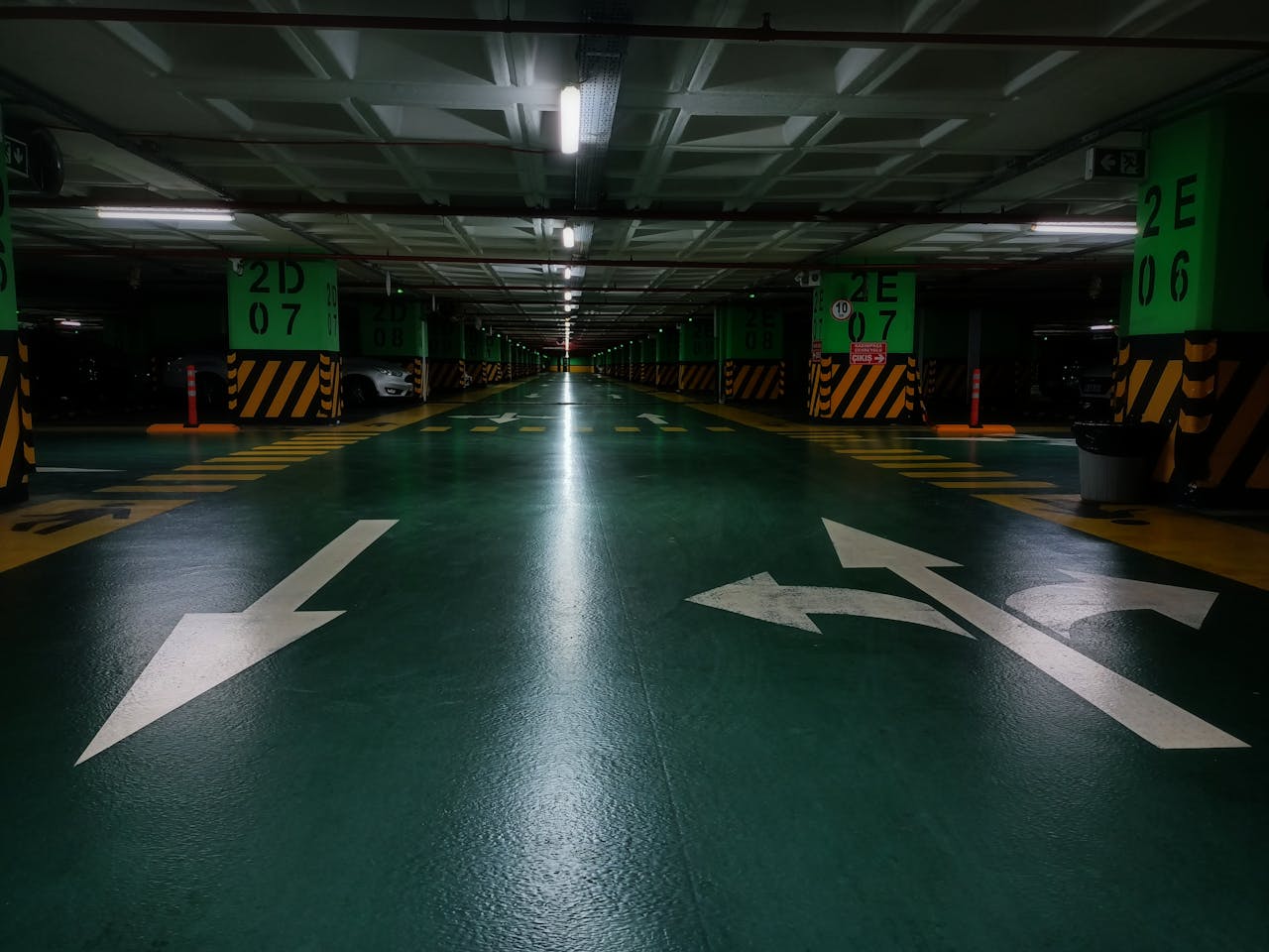 about-02 Dimly lit underground parking lot with directional arrows and green floor marking.