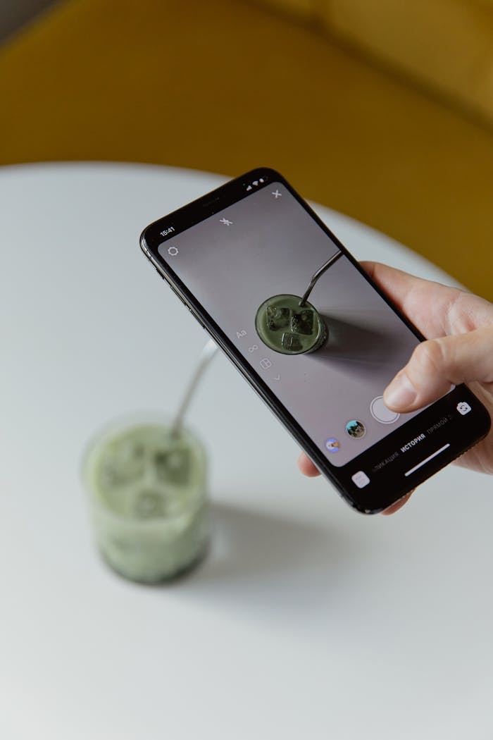 A smartphone capturing an iced matcha latte on a table.